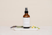 Bottle of Iyy & Sage product on a marble tray with lavender and flowers on a beige background