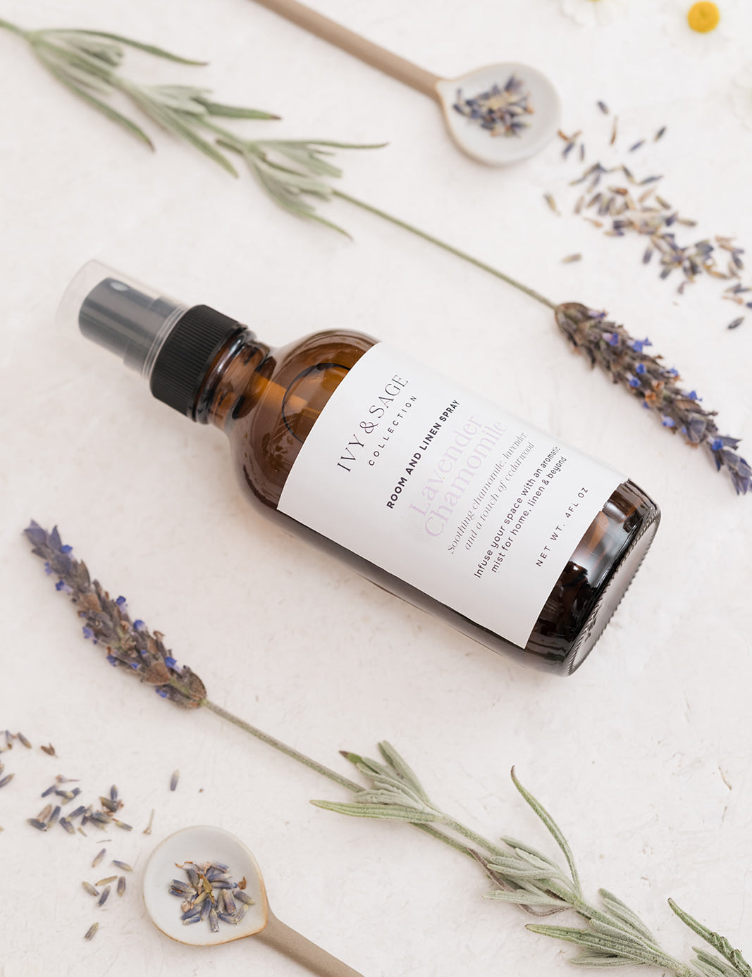 A bottle of Ivy & Sage spray with lavender and flowers on a light background