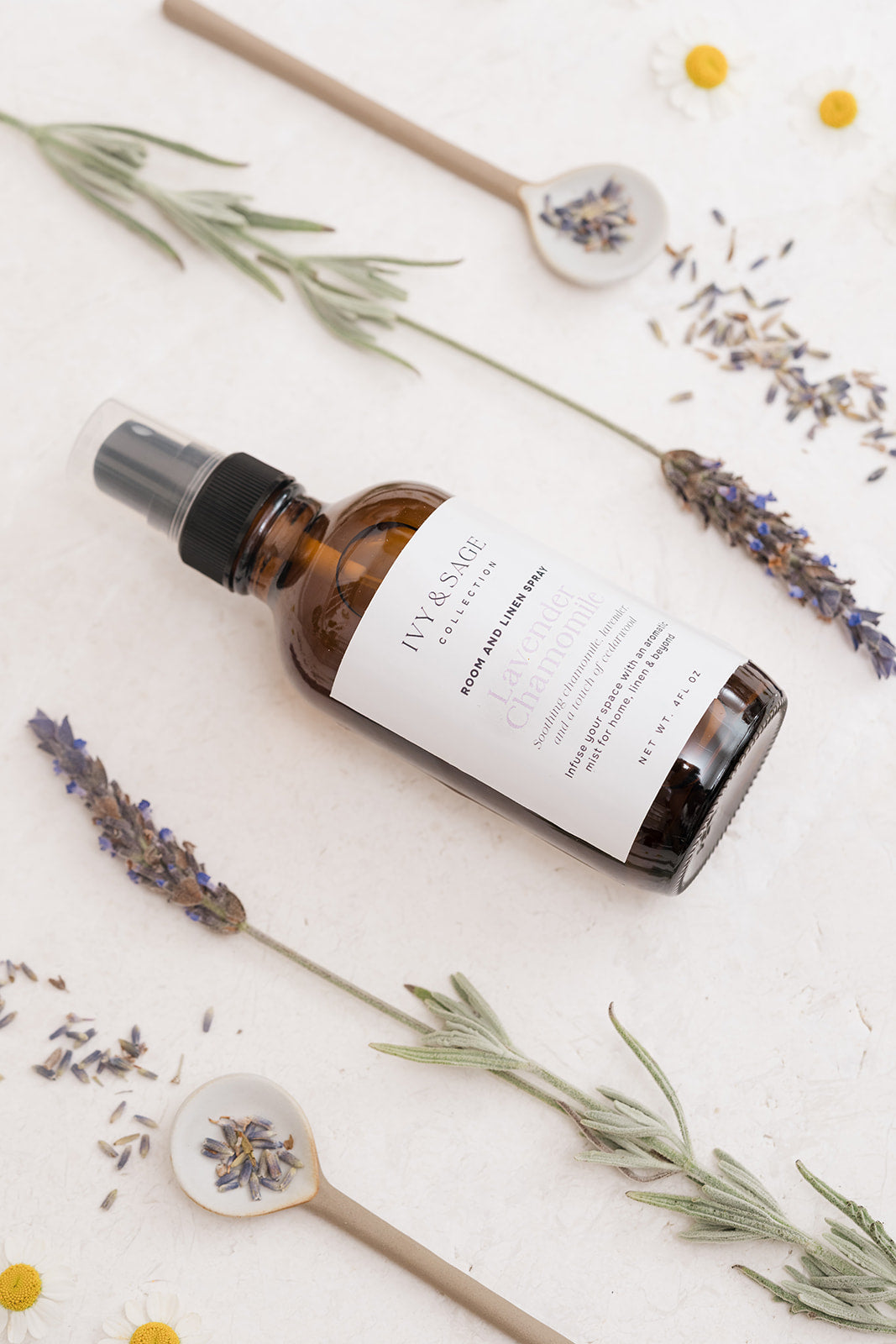 A bottle of Ivy & Sage spray with lavender and flowers on a light background