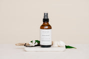 Room & Linen Spray bottle on a white surface with decorative elements such as vanilla and sea shells