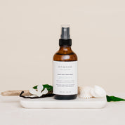 Room & Linen Spray bottle on a white surface with decorative elements such as vanilla and sea shells