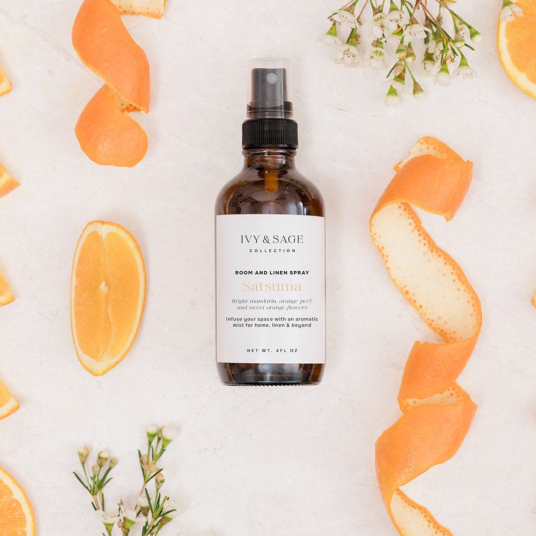 Bottle of Room & Linen Spray surrounded by orange slices and peels on a light background