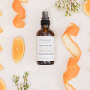 Bottle of Room & Linen Spray surrounded by orange slices and peels on a light background