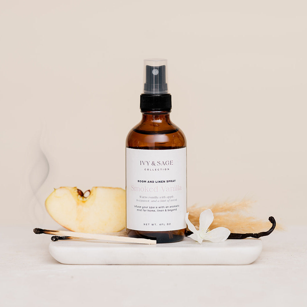 Bottle of 'Ivy & Sage' product on a white plate with candles and a spoon on a beige background in Smoked Vanilla Scent