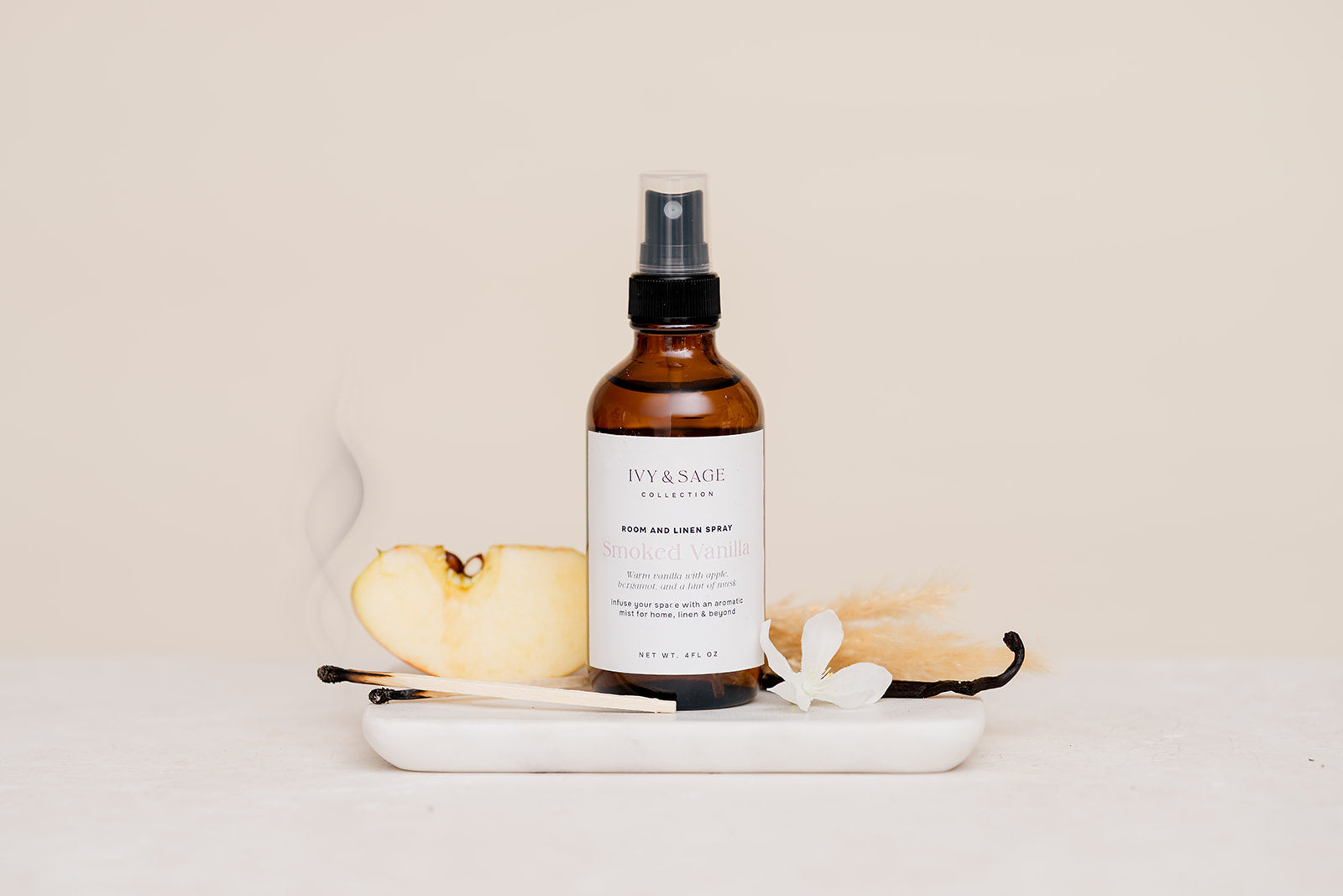 Bottle of Ivy & Sage Room & Linen Spray on a white plate with apple, vanilla and a smokey match