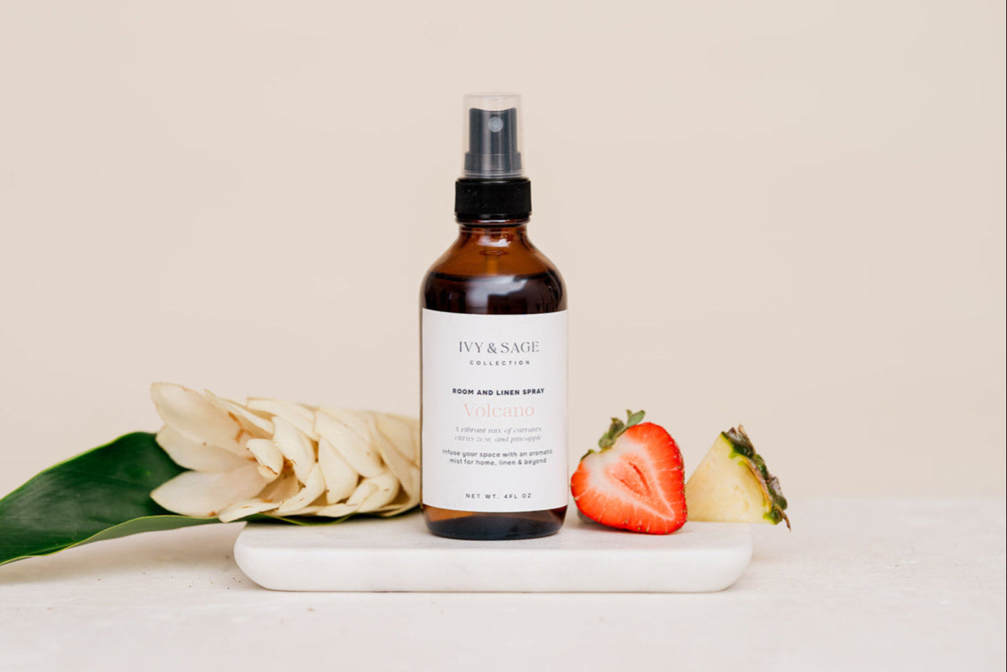 Bottle of Room & Linen Spray on a white surface with flowers, strawberry and pinappe