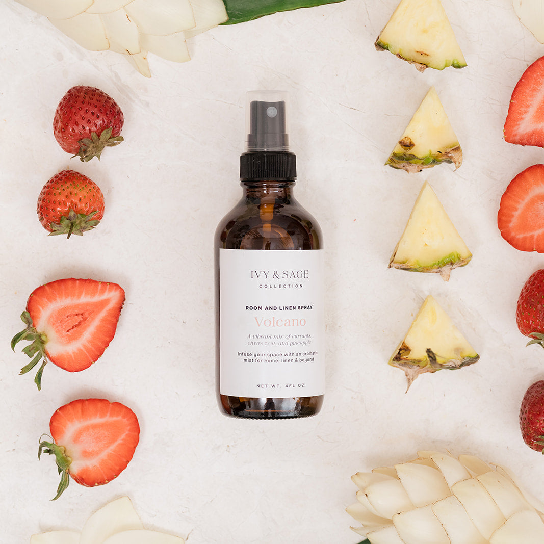 Bottle of Room & Linen pray on a white background with sliced pineapples and strawberries.