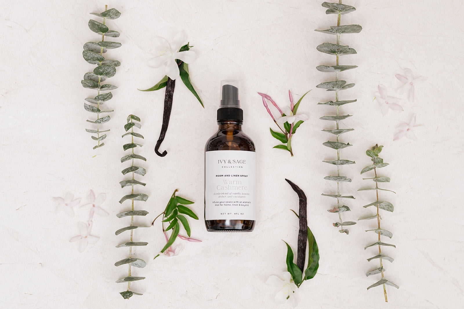 Room & Linen Spray bottle with vanilla beans and eucalyptus leaves on a light background