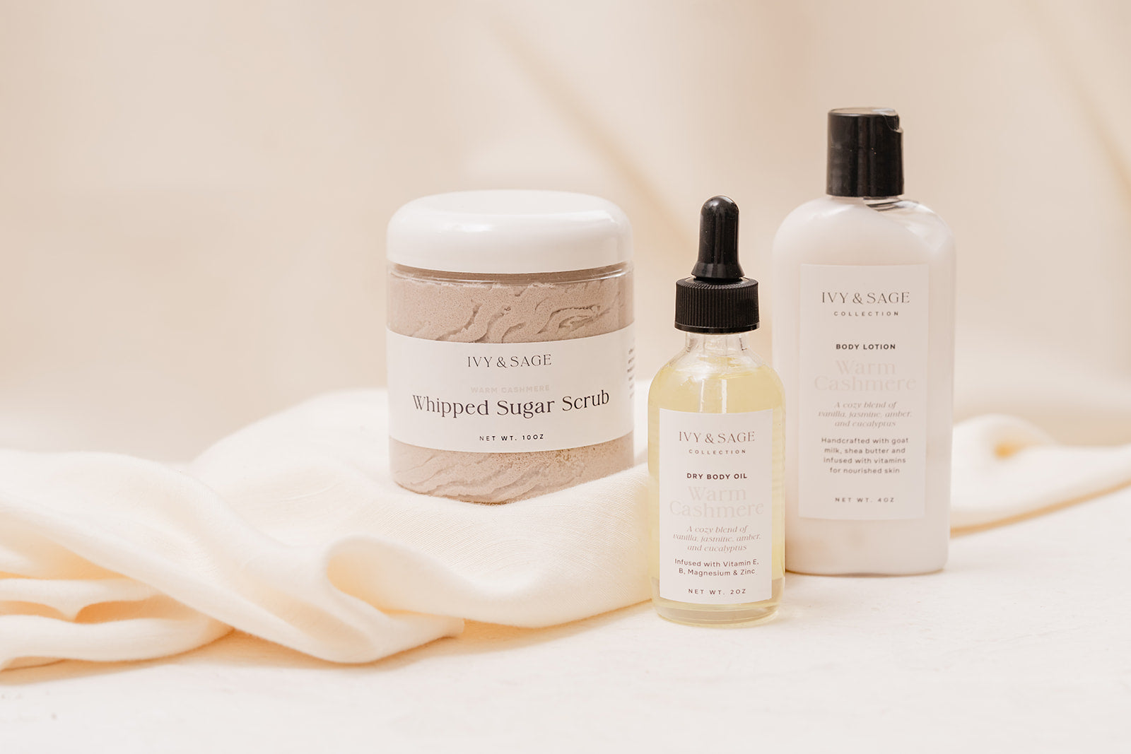 Ivy & Sage skincare products including a jar, dropper bottle, and lotion on a soft fabric background.