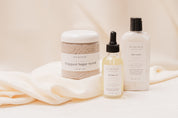 Ivy & Sage skincare products including a jar, dropper bottle, and lotion on a soft fabric background.