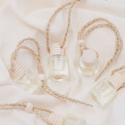 Small glass car diffuser with an adjustable rope and a bundle of pine needles on a white marble slab against a beige background. Car Freshener that smells like Christmas. Christmas scents perfect gift idea. 