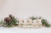 Small glass car diffuser with an adjustable rope and a bundle of pine needles on a white marble slab against a beige background. Car Freshener that smells like Christmas. Christmas scents perfect gift idea. 