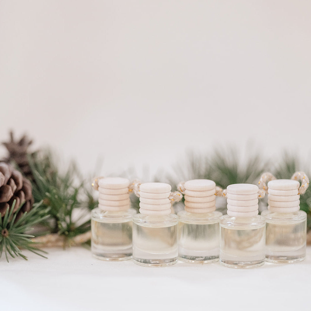 Small glass car diffuser with an adjustable rope and a bundle of pine needles on a white marble slab against a beige background. Car Freshener that smells like Christmas. Christmas scents perfect gift idea. 