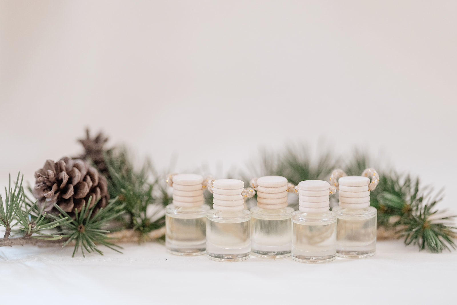 Small glass car diffuser with an adjustable rope and a bundle of pine needles on a white marble slab against a beige background. Car Freshener that smells like Christmas. Christmas scents perfect gift idea. 