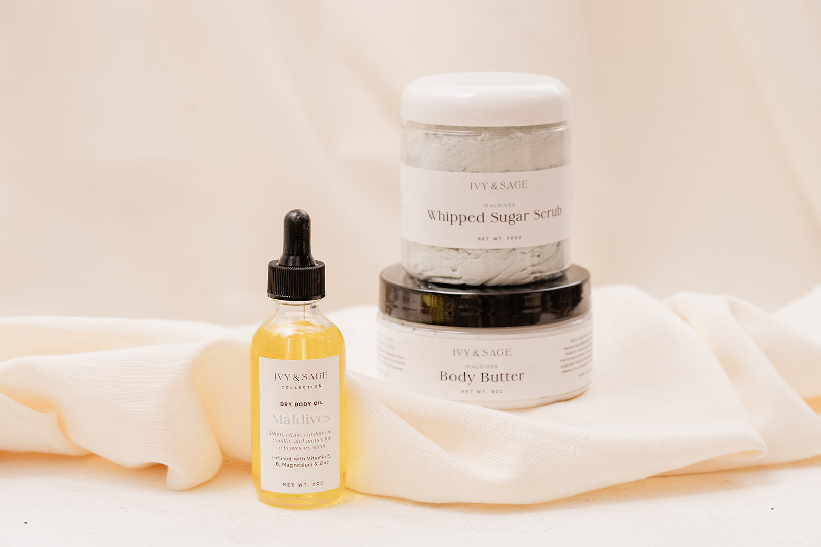 IVY & SAGE skincare products including a body oil, sugar scrub and body butter on a beige background