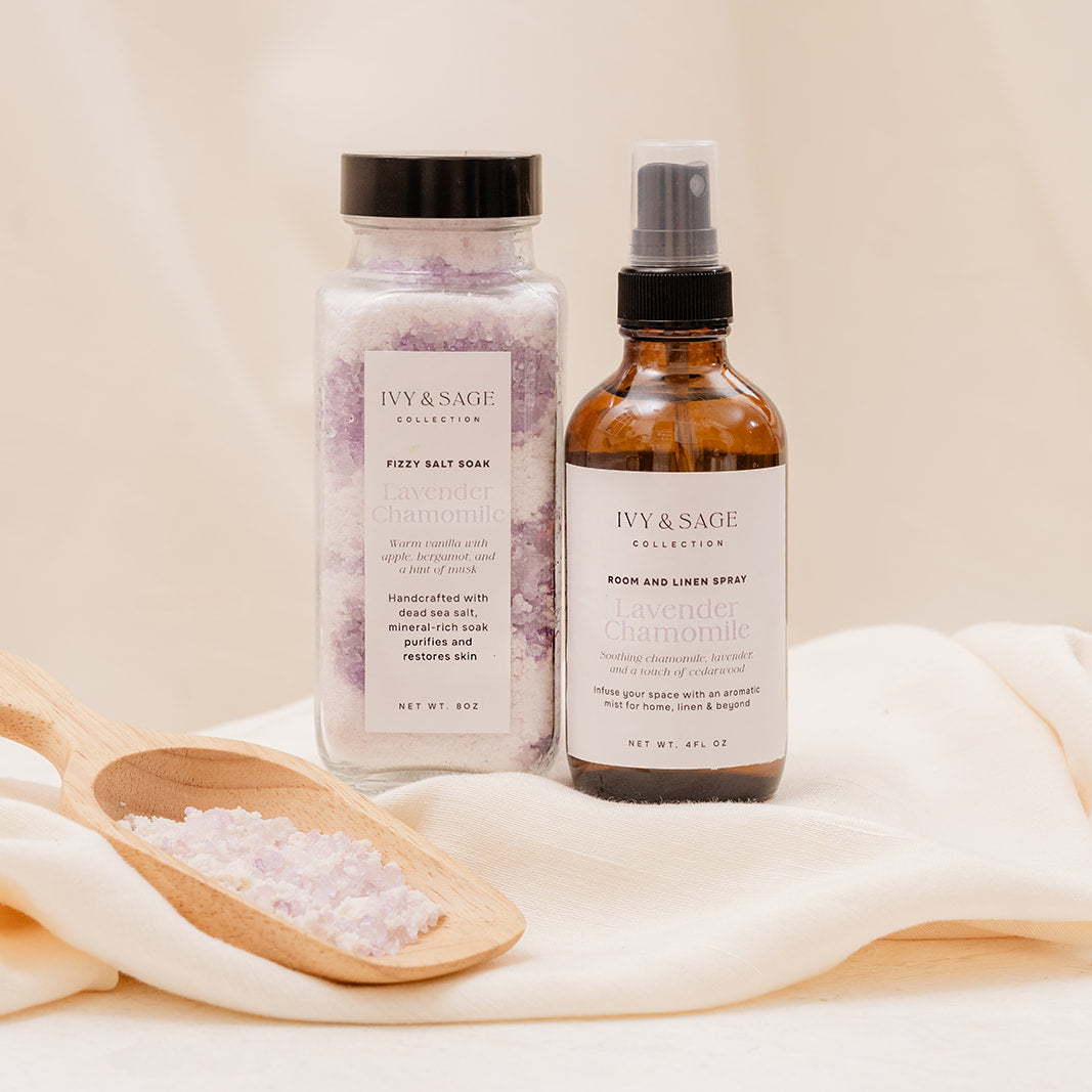 Two bottles of Ivy & Sage Bath Salts and Room Spray products on a light fabric background