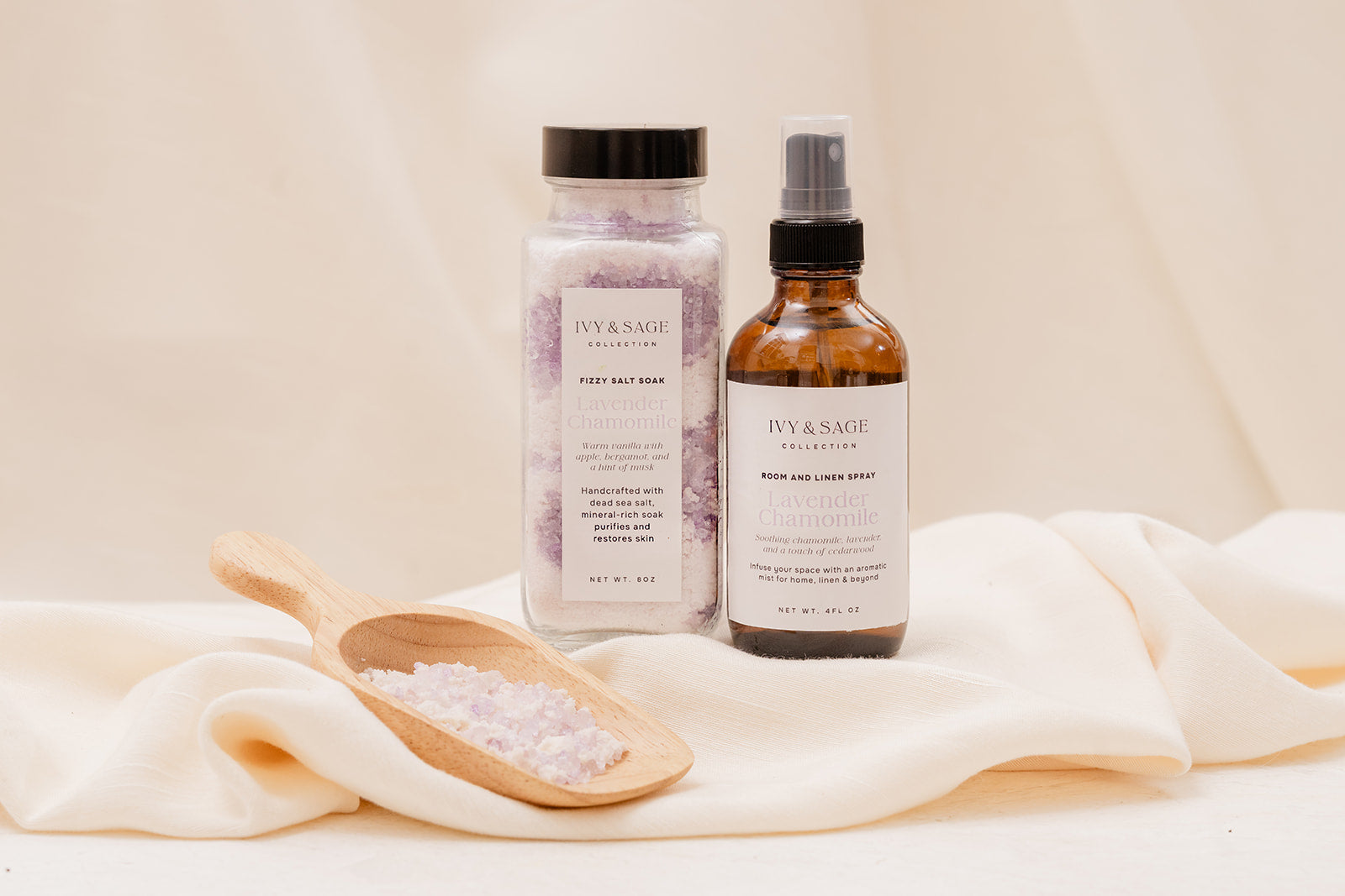 Two bottles of Ivy & Sage Bath Salts and Room Spray products on a light fabric background