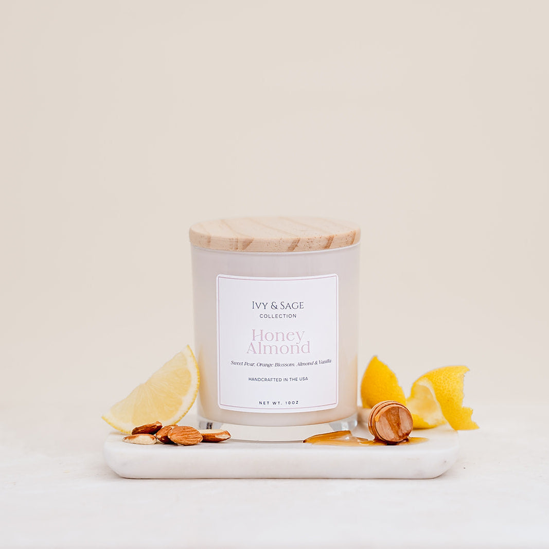 Ivy & Sage Honey & Almond glass candle with wooden lid, styled with lemon, almonds and honey.