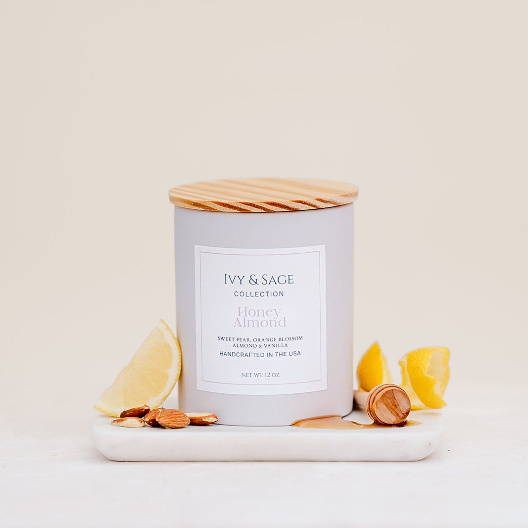 Ivy & Sage Honey & Almond ceramic candle with wooden lid, styled with lemon and almonds.