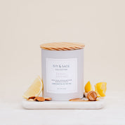 Ivy & Sage Honey & Almond ceramic candle with wooden lid, styled with lemon and almonds.