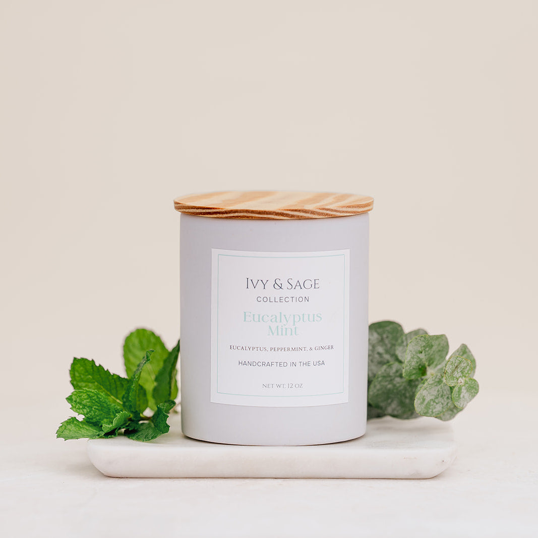 Ivy & Sage Eucalyptus Mint ceramic candle with wooden lid, styled with fresh mint and eucalyptus leaves.