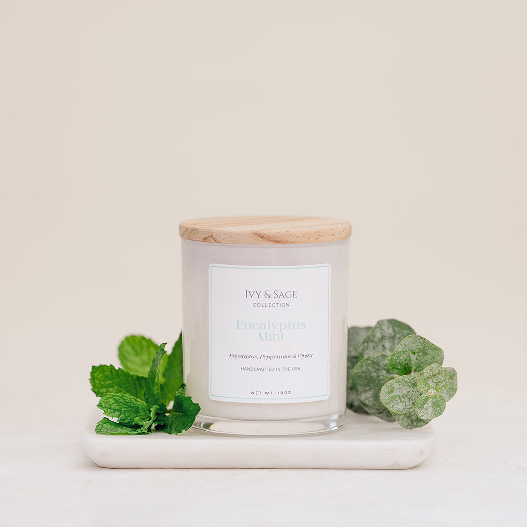 Ivy & Sage Eucalyptus Mint glass candle with wooden lid, styled with fresh eucalyptus and mint leaves.”