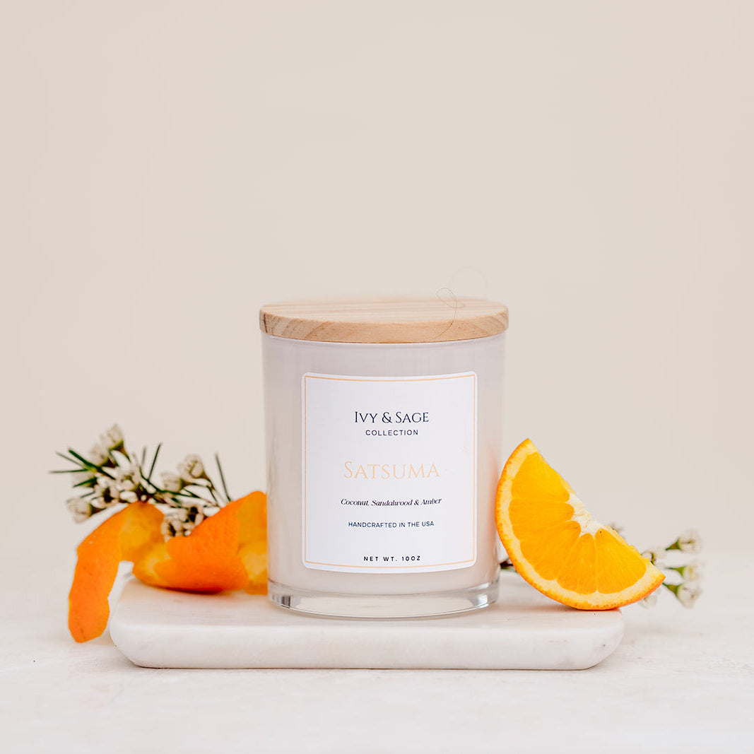 Ivy & Sage Satsuma glass candle with wooden lid, styled with fresh orange and orange blossom.