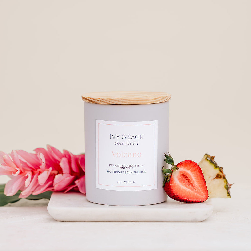 Ivy & Sage Volcano ceramic candle with wooden lid, styled with pineapple, strawberry and tropical floral details.