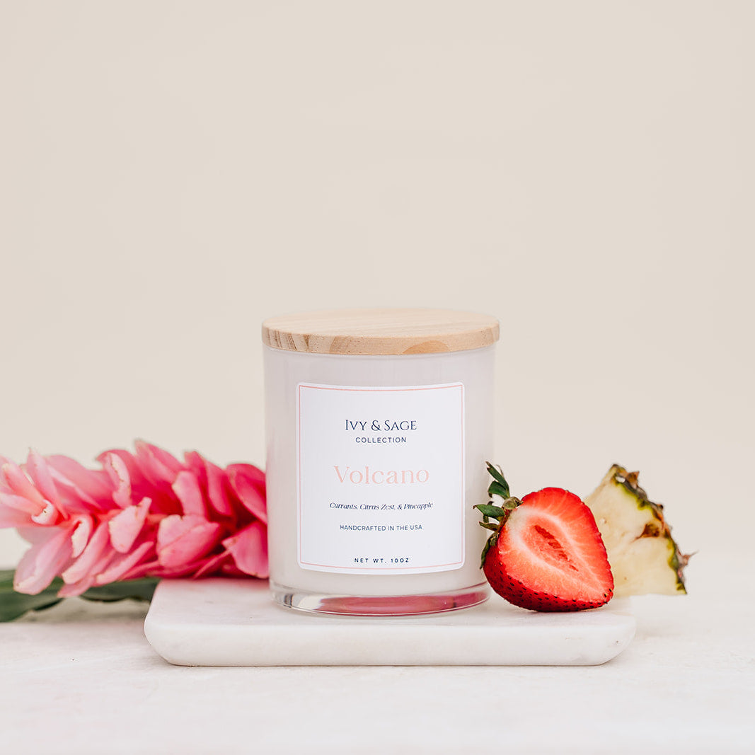 Ivy & Sage Volcano glass candle with wooden lid, styled with strawberry, pineapple and pink florals.
