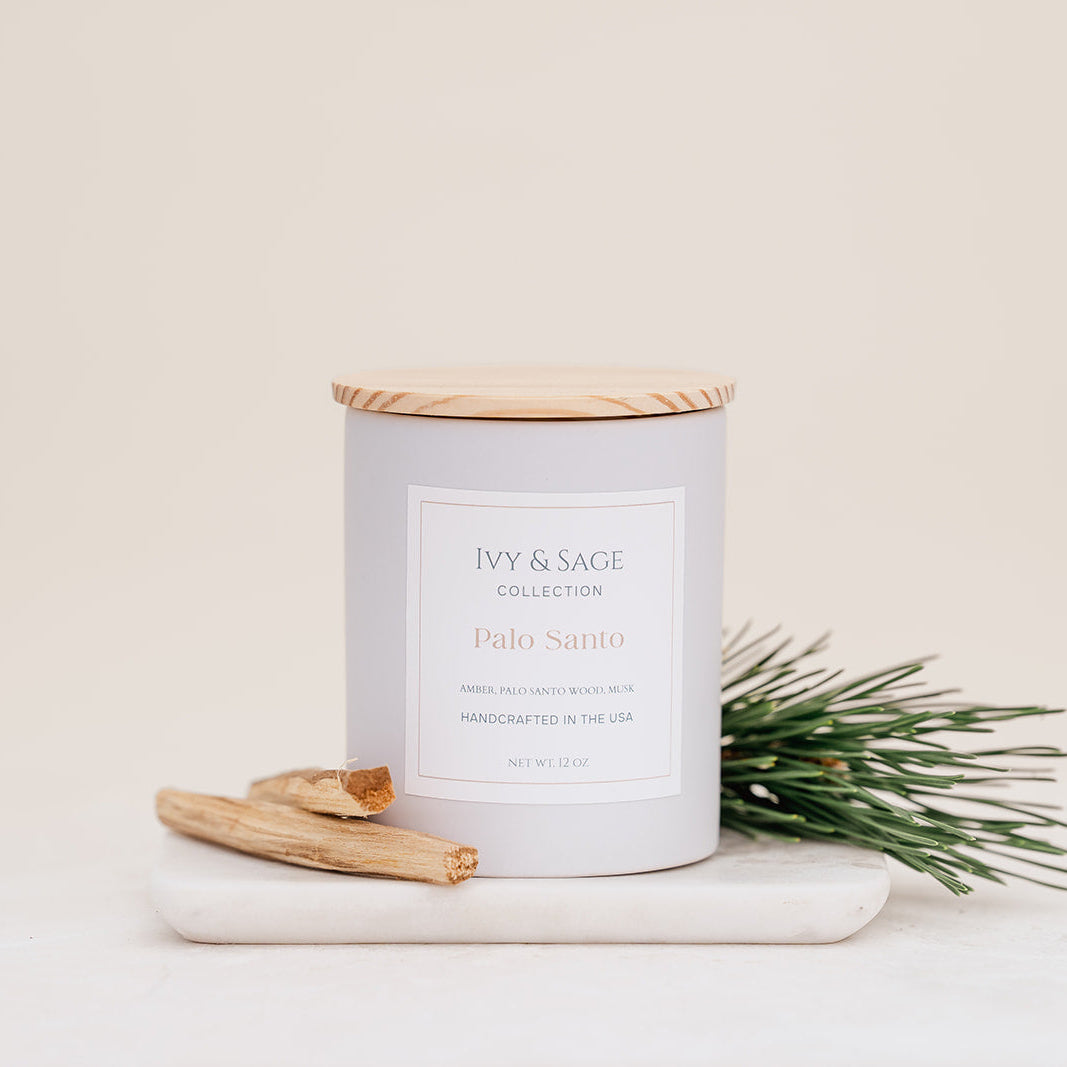 Ivy & Sage Palo Santo ceramic candle with wooden lid, styled with palo santo wood and fresh greenery.
