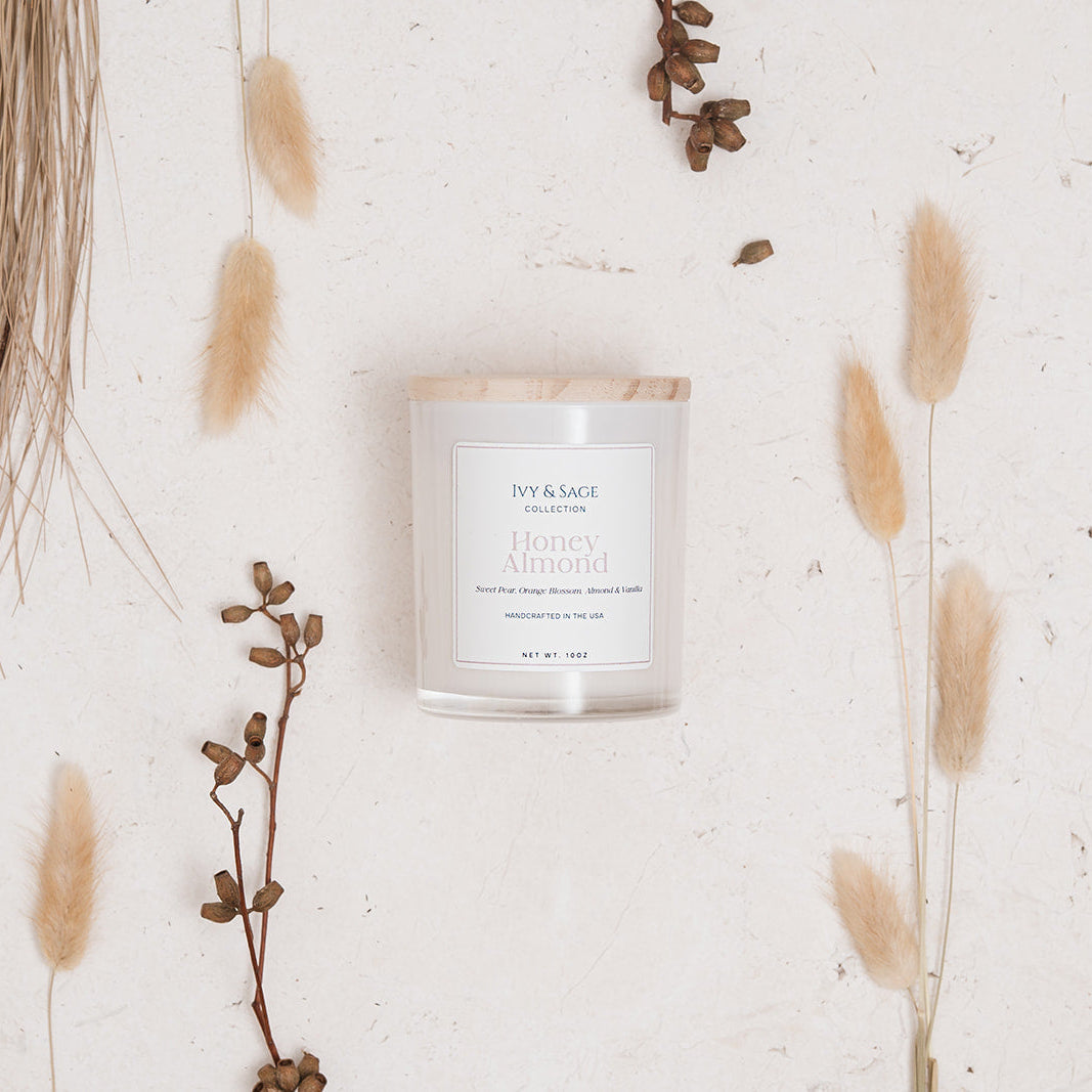Ivy & Sage Honey & Almond glass candle flat lay styled with warm neutral botanicals.
