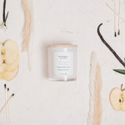 Ivy & Sage Smoked Vanilla glass candle flat lay styled with apple, vanilla and neutral botanicals.