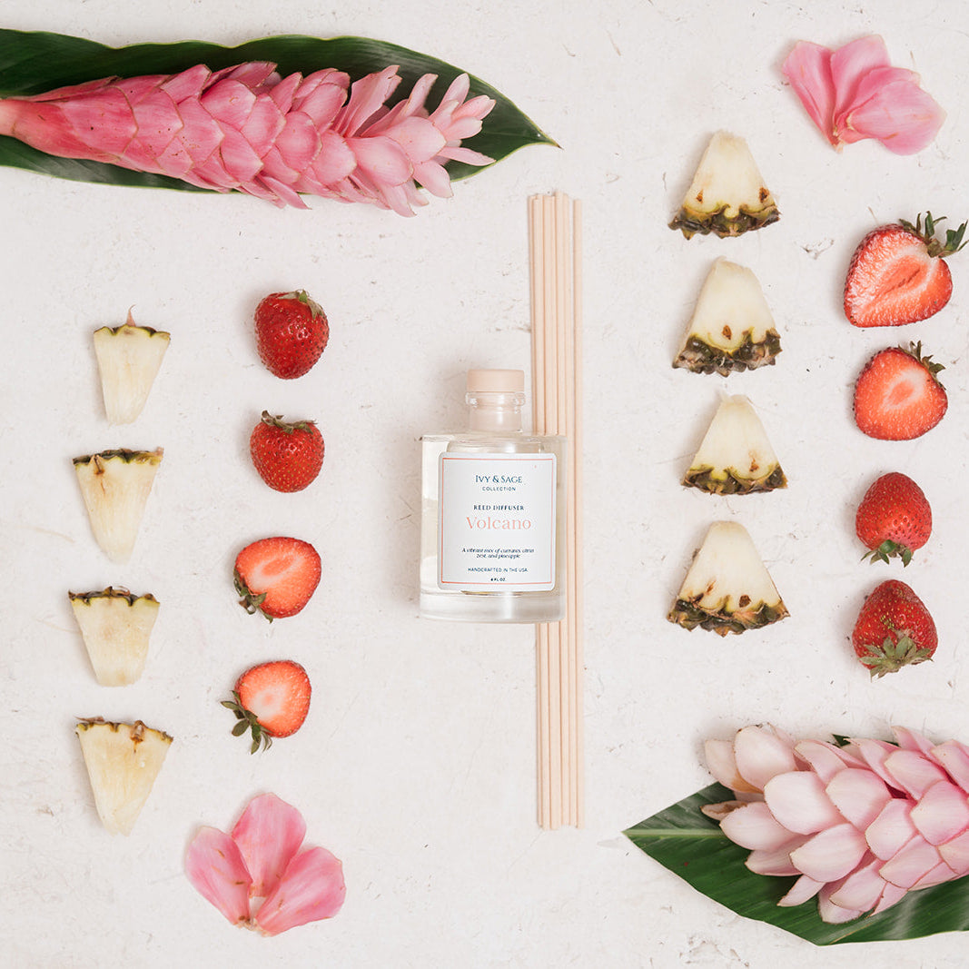 Ivy & Sage Volcano reed diffuser styled in a vibrant flat lay with strawberry, pineapple and tropical floral details.