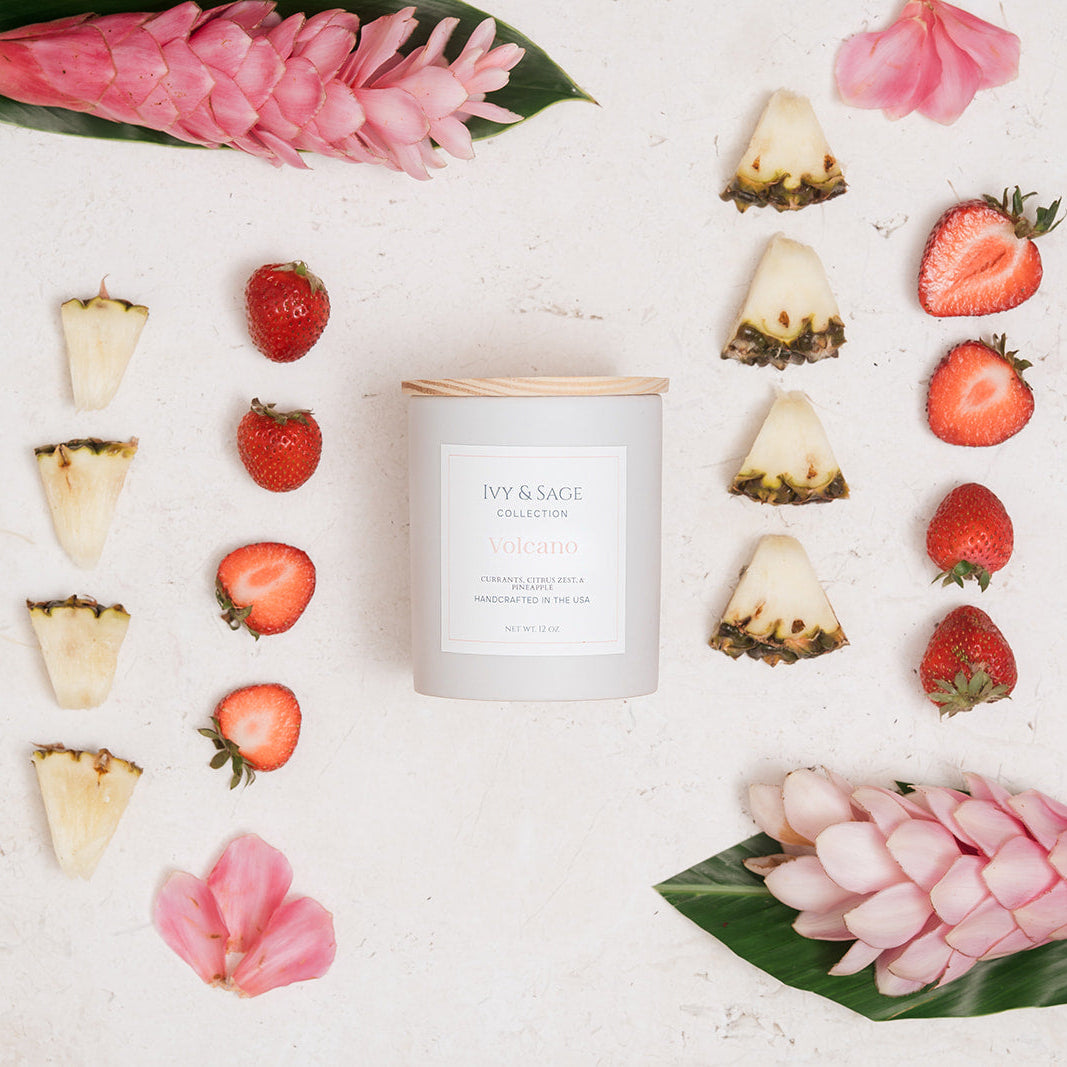 Ivy & Sage Volcano ceramic candle flat lay surrounded by pineapple, strawberries and tropical flowers.