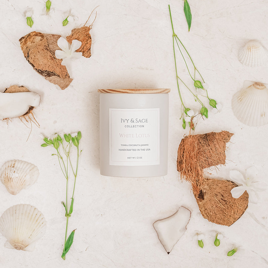 Ivy & Sage White Lotus ceramic candle styled in a botanical flat lay with coconut and white flowers.