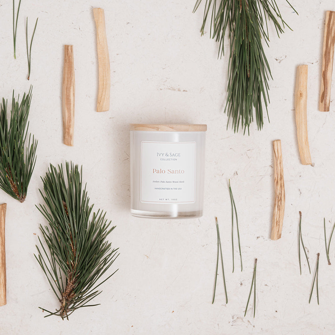 Ivy & Sage Palo Santo glass candle flat lay styled with palo santo wood and pine greenery.